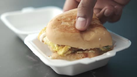 hand holding a takeaway egg burger in a styrofoam container