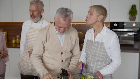 gruppe fröhlicher älterer freunde, die in der küche kochen, während sie lachen und reden