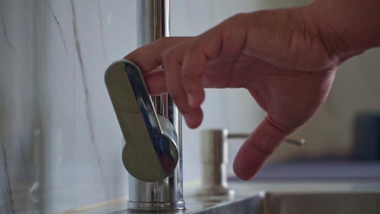 Water tap being switched on by hand in a kitchen sink area. Sustainable living, water saving, hygiene, and responsible consumption concept.