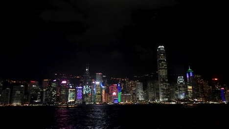 Wide-view-of-famous-Hong-Kong-skyline-and-Victoria-Harbor-at-night-with-bright-city-lights,-boats-and-ferries-passing-by-on-harbor