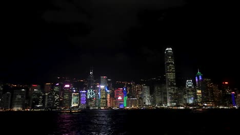 wide view of famous hong kong skyline and victoria harbor at night with bright city lights, boats and ferries passing by on harbor