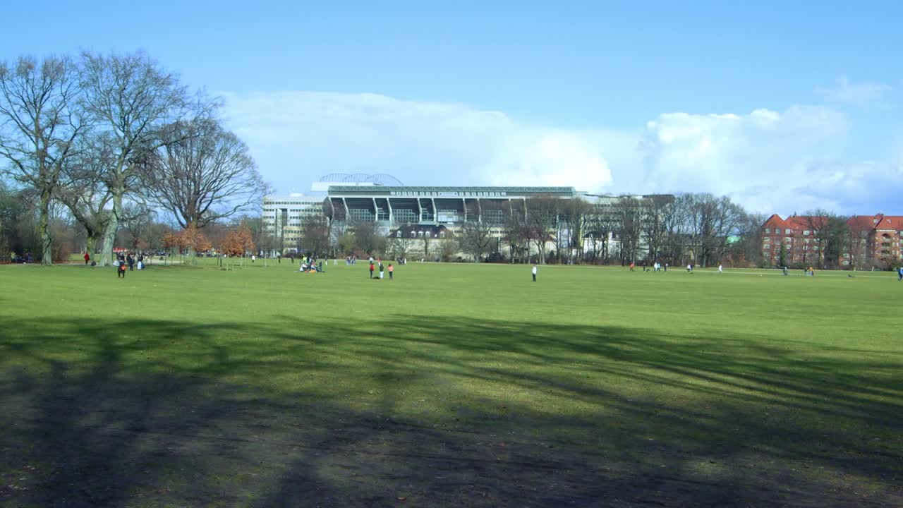 People on lawn in front of stadium with blue sky - Copenhagen Spring Park – Copenhagen Fælledparken - 4K Ultra HD UHD
