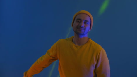 the man dances merrily and looks at the camera in the light of strobe lights and colored spotlights. neon colors and crazy man dancing to music and singing in a yellow jacket and hat