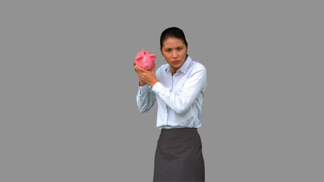 businesswoman shaking an empty piggy bank on grey screen