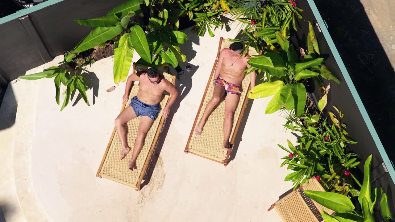 Aerial View of Two Men Sunbathing on Loungers in Tropical Setting