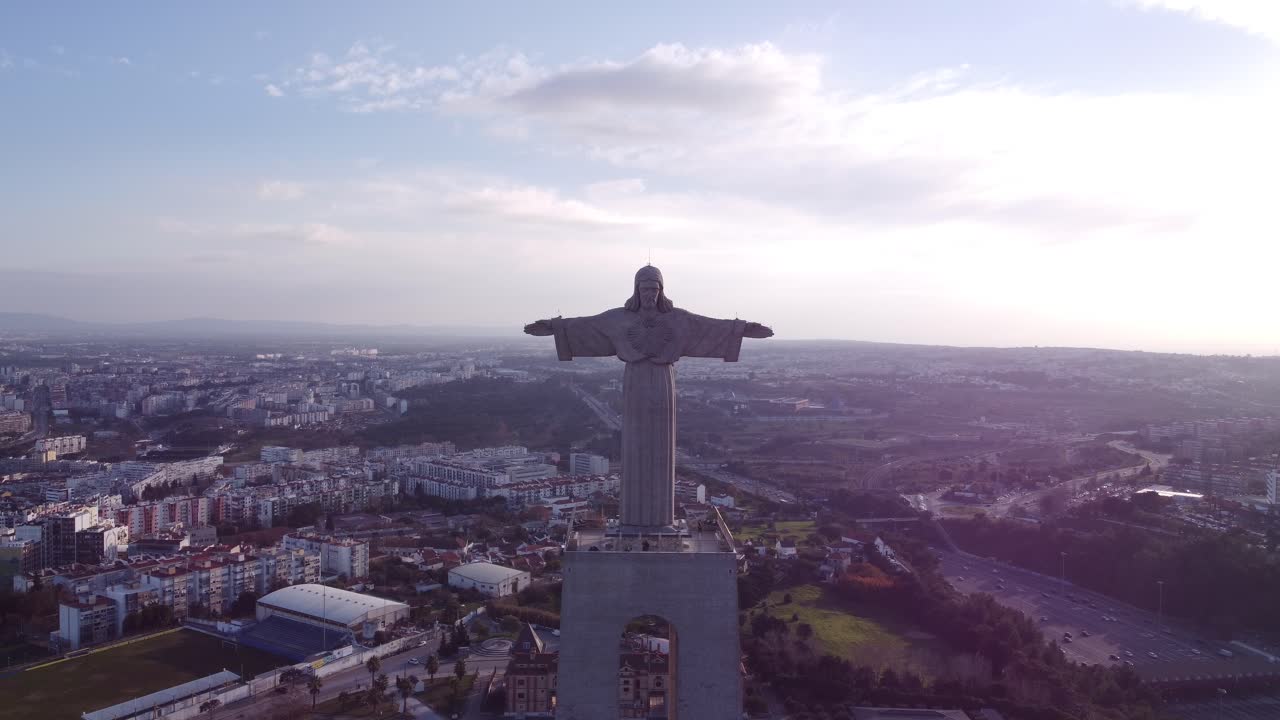 vuelo de drones estacionario y acercándose al rostro de cristo cristo rei en portugal lisboa al atardecer con la ciudad en la espalda