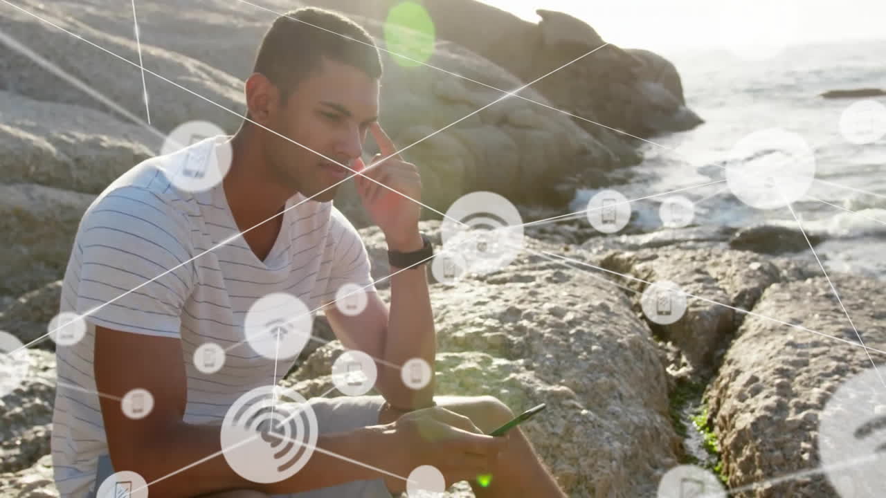 animación de la red de conexiones con iconos sobre hombre biracial usando teléfono inteligente por mar