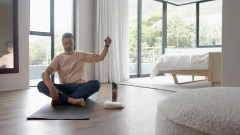 relaxed senior biracial man practicing yoga sitting floor at home, copy space, slow motion