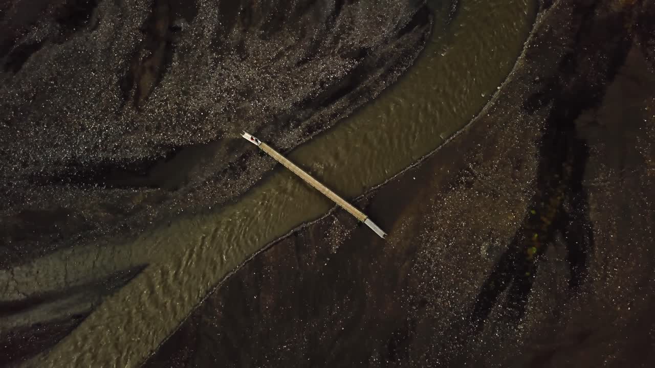 Aerial drone view of people crossing a bridge, over a river flowing in the Fimmvörðuháls area, Iceland