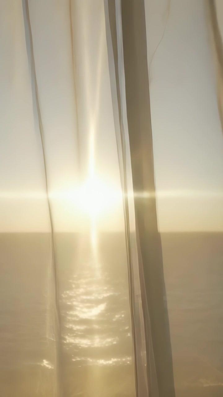 Video verticale: Panoramica della telecamera che mostra tende velate che si aprono, rivelando il sole sul mare in una stanza, con un bagliore.