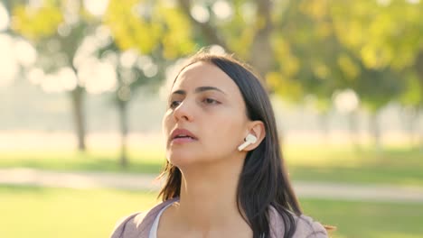una joven india corriendo con auriculares puestos en un parque por la mañana.