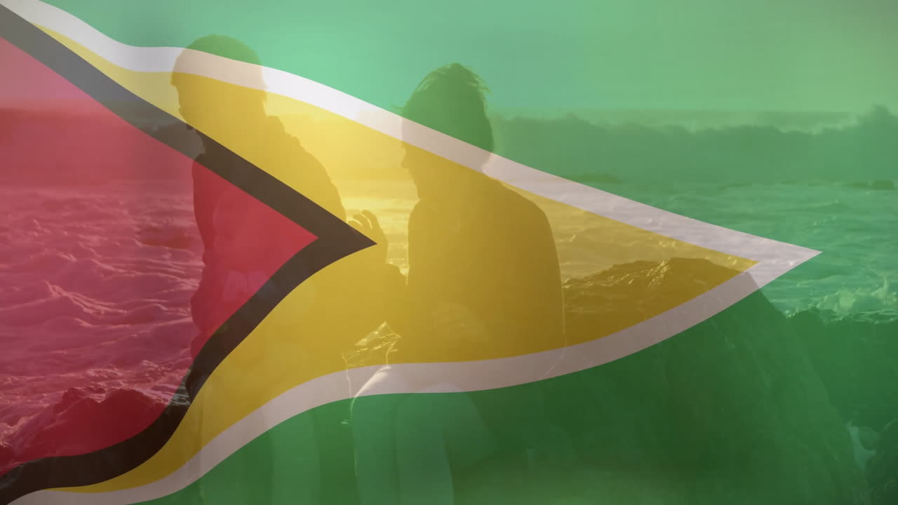 Guyana flag overlay on silhouetted people by ocean at sunset animation