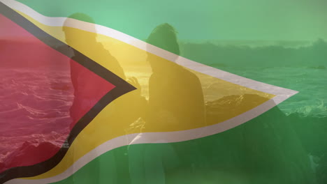 guyana flag overlay on silhouetted people by ocean at sunset animation
