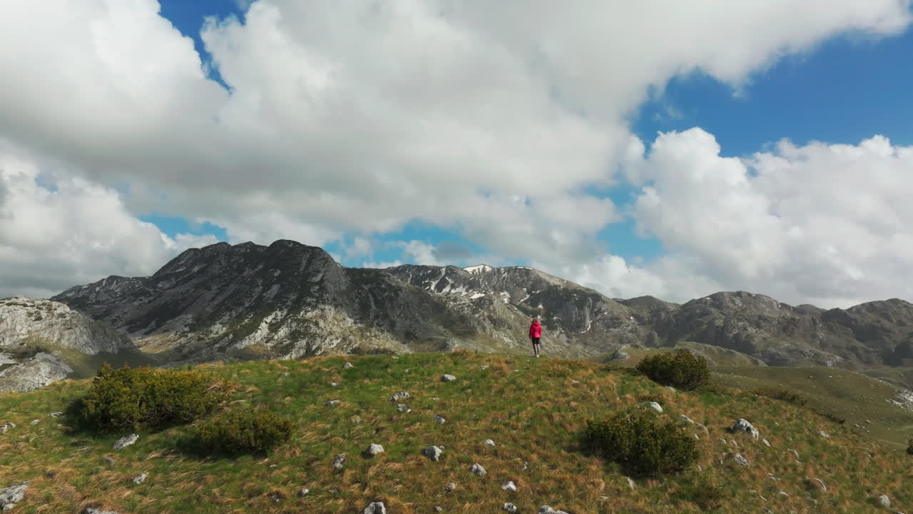 Scandinavian woman admire remote Montenegro mountains from hilltop; drone reveal