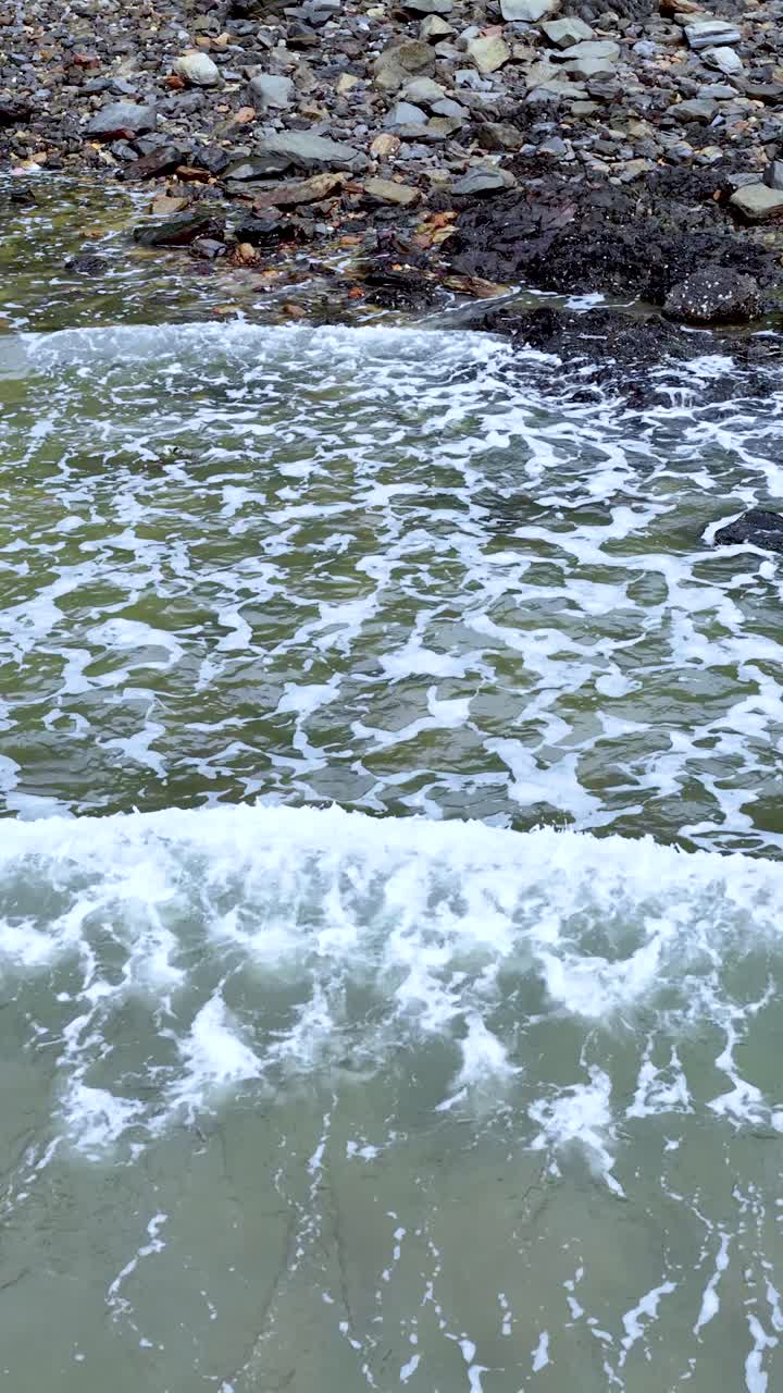 Ondas oceânicas espumosas quebram contra a costa rochosa, luz do dia, câmera estável, ambiente marinho natural