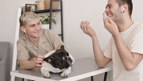 two men sitting at table and petting dog