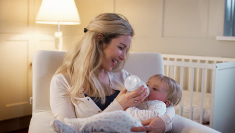 mother in nursery feeding baby daughter from bottle