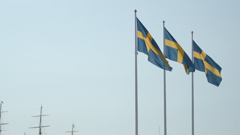 static view of three swedish flags moving in wind by sailboat masts