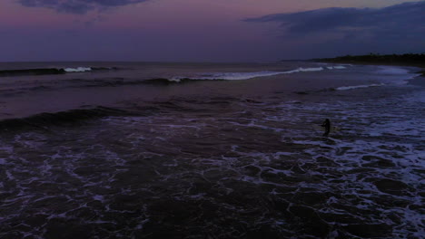 v2 a surfer girl fighting with the waves while pedalling in the ocean in the dark at sunrise. she is keep pushing forward despite the waves that pushed her back! bali, indonesia