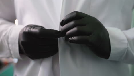 a close-up view of a man wearing black gloves buttoning his lab coat step by step