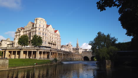 Zeitraffer-Des-Empire-Hotels,-Pulteney-Weir---Pulteney-Bridge-In-Bath,-Somerset-An-Einem-Wunderschönen-Sommermorgen-Mit-Blauem-Himmel-Und-Goldenem-Licht