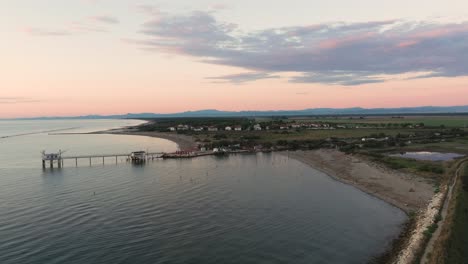 Luftaufnahme-Von-Fischerhütten-Am-Ufer-Der-Mündung-Bei-Sonnenuntergang,-Italienische-Fischermaschine,-Genannt-&quot;Trabucco&quot;,-Lido-Di-Dante,-Ravenna-In-Der-Nähe-Des-Comacchio-Tals