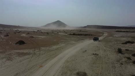 aerial view of dust trail from 4x4 driving across arid desert landscape with mud volcano in background