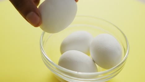 video of close up of biracial man putting egg into bowl on yellow background