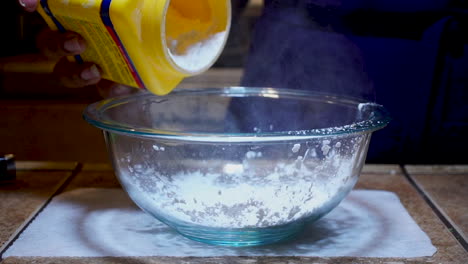 pouring cornmeal or corn flour into glass mixing bowl, slow motion close up