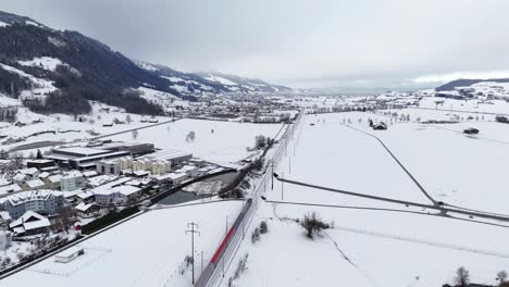 Vista-Aérea-Que-Muestra-El-Tren-A-Caballo-En-El-Ferrocarril-En-El-Paisaje-Invernal-Nevado-Y-El-Paso-Subterráneo-De-Los-Automóviles---Reichenburg,-Suiza