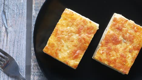 two square baked cheese custard dishes on a black plate