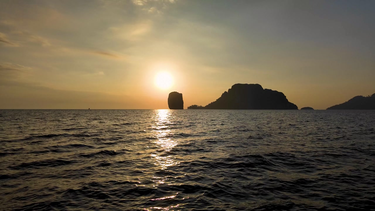 Warm sunset over Andaman Sea in Krabi Thailand with island silhouettes and shimmering reflections on gentle waves creating calm tropical evening atmosphere