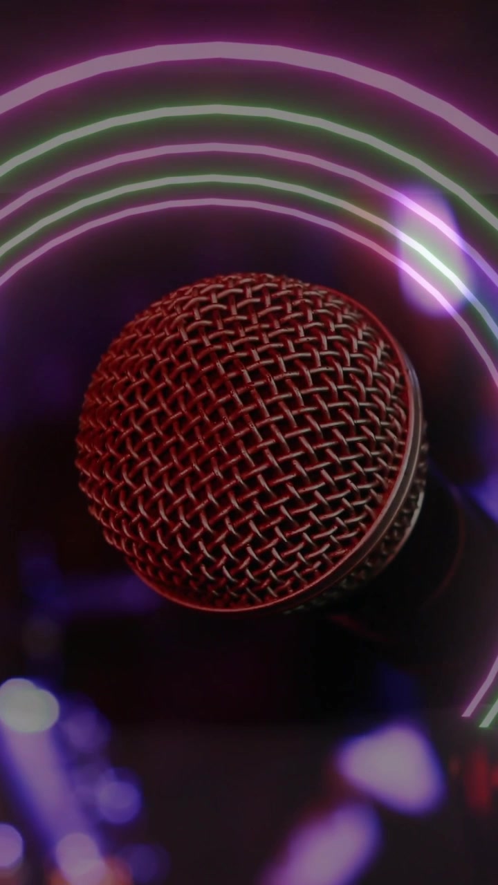 Vertical video: Handheld mic sliding left to center, focusing, neon rings framing grille for music