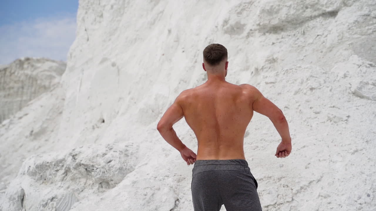 Back view of athlete with muscular body outdoors. Healthy body of a bodybuilder on white mountain background.