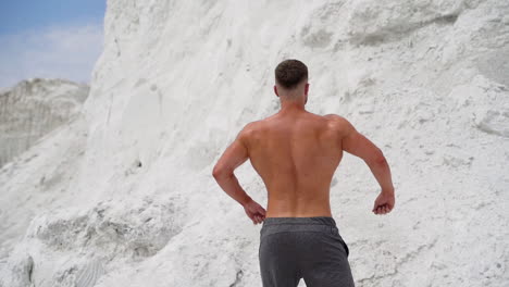back view of athlete with muscular body outdoors. healthy body of a bodybuilder on white mountain background.