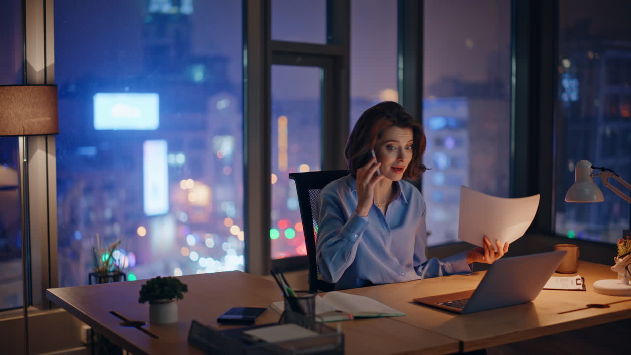 Frustrated professional talking smartphone at dark office holding papers