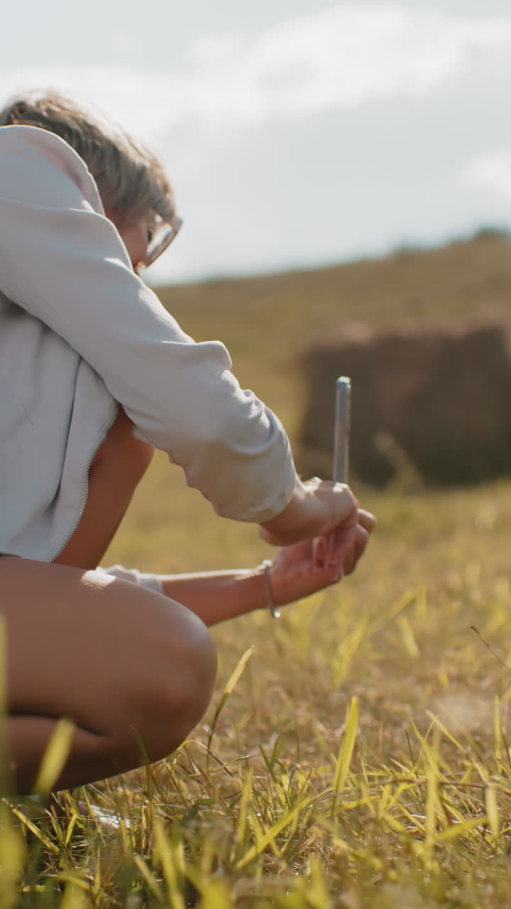 turista femenina en cuclillas mientras captura una fotografía de alguien en una vasta tierra de cultivo, la luz del sol destaca la hierba dorada, las colinas onduladas y el paisaje rústico del campo