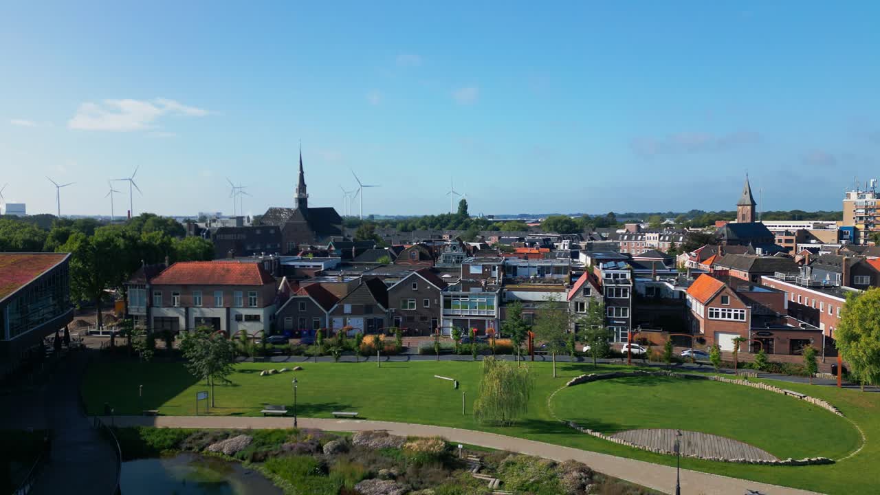Wide shot of Coevorden city park with modern sculpture, green grass, pond, and church towers in background. Captured in Coevorden, Drenthe, Netherlands (Coevorden, Drenthe, Nederland)
