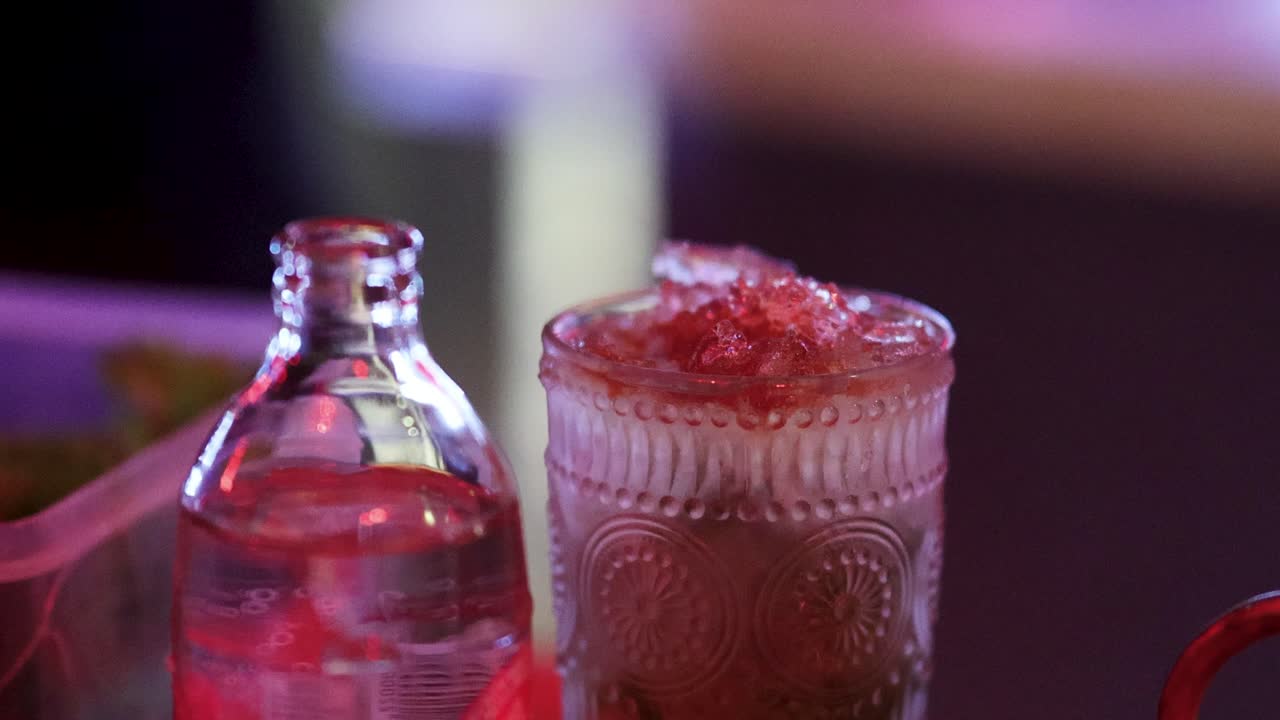 Bartender adds bitters to cocktail in ornate glass, vibrant bar lighting, close-up, steady camera