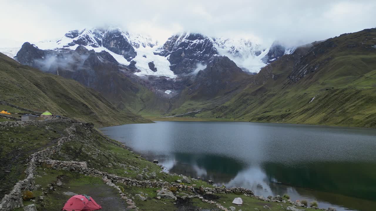 Flyover camp tents at alpine tarn toward mtn peaks on opposite shore