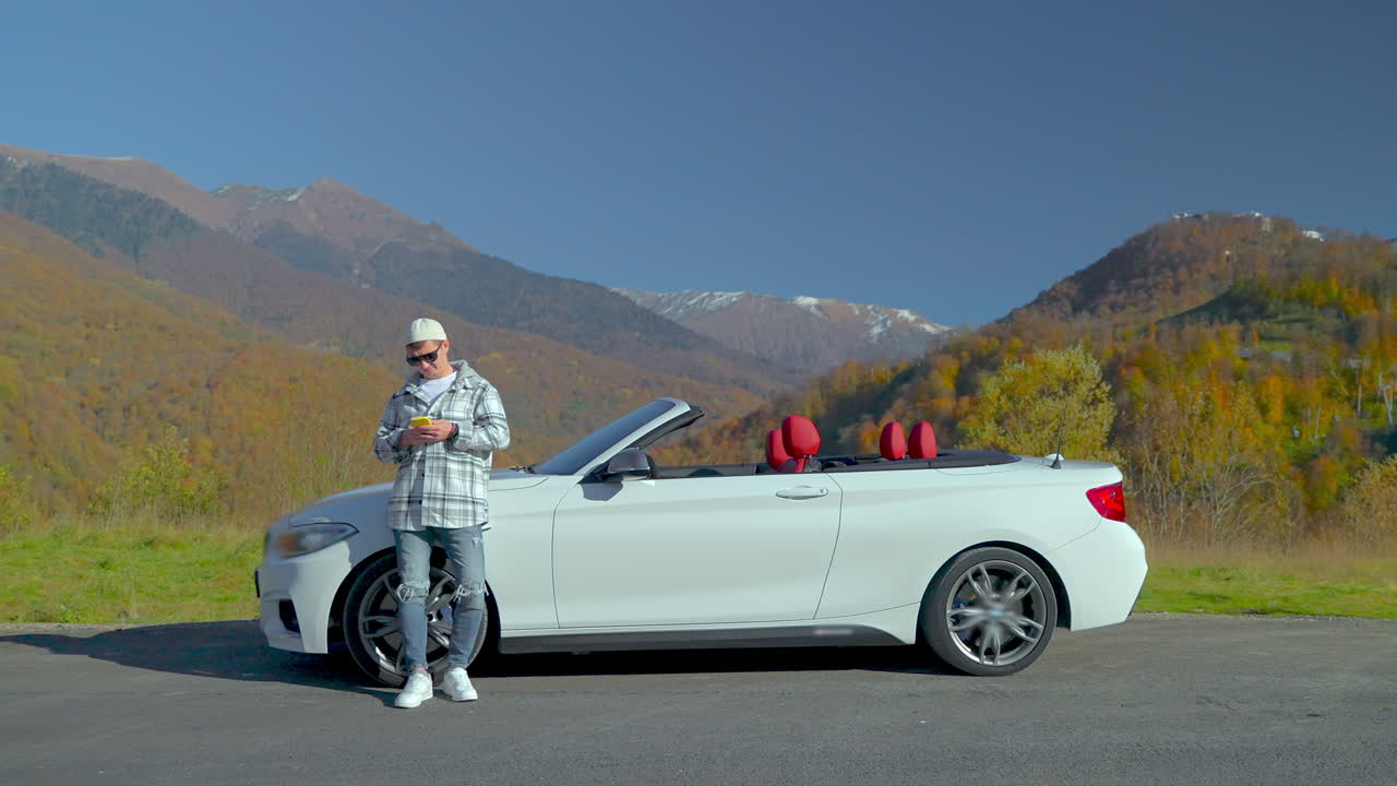 hombre usando el teléfono al lado de un coche descapotable blanco en las montañas durante el otoño