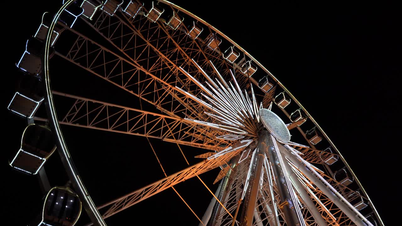 Ferris wheel. A ferris wheel rotates against the background of the night sky. Close-up of a Ferris wheel with night illumination. lluminated Ferris Wheel construction rotating against dark night sky background.