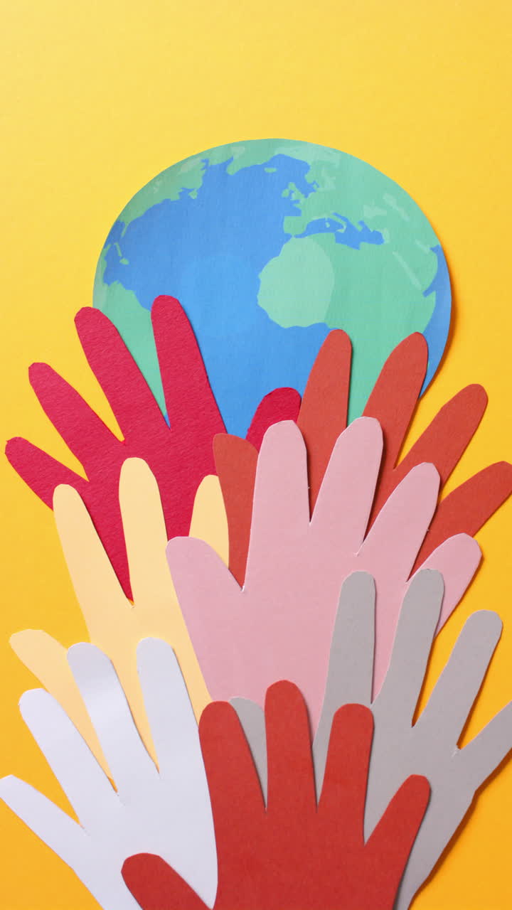 Vertical video of hands with globe made of colourful paper on yellow background with copy space