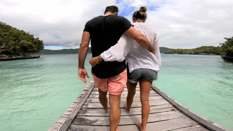 una pareja caminando por un muelle de madera en una isla tropical