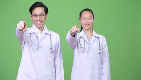 young asian couple doctors pointing at camera together
