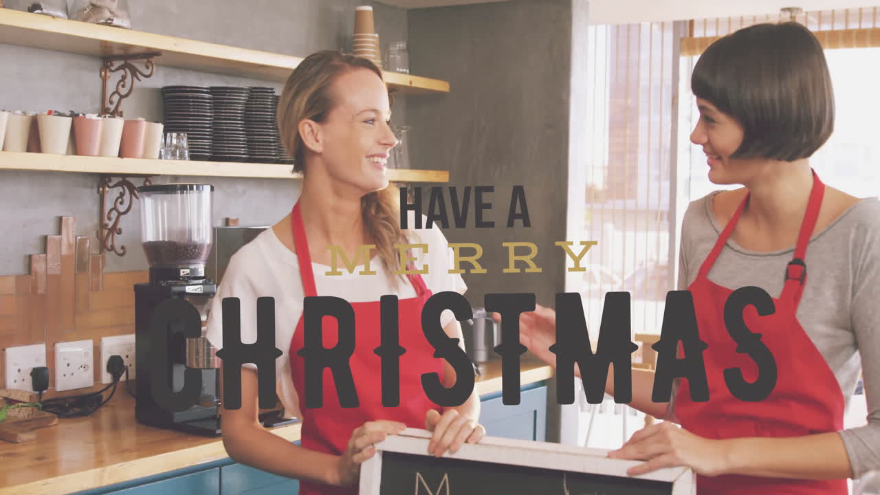 Wearing red aprons, two women in kitchen with animation Have Merry Christmas