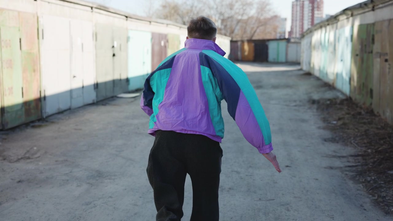 Un singolo inseguitore che corre attraverso un vicolo di garage con una giacca viola, scatto determinato, postura concentrata, urbano vuoto.