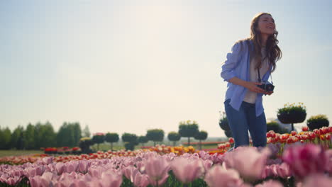 Happy-woman-touching-flowers-at-walk-with-camera-in-tulip-field-in-sunny-day.