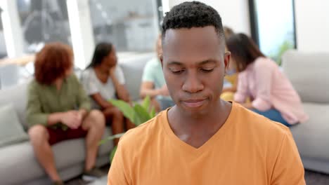 emotional man with diverse friends talking in background during group therapy session