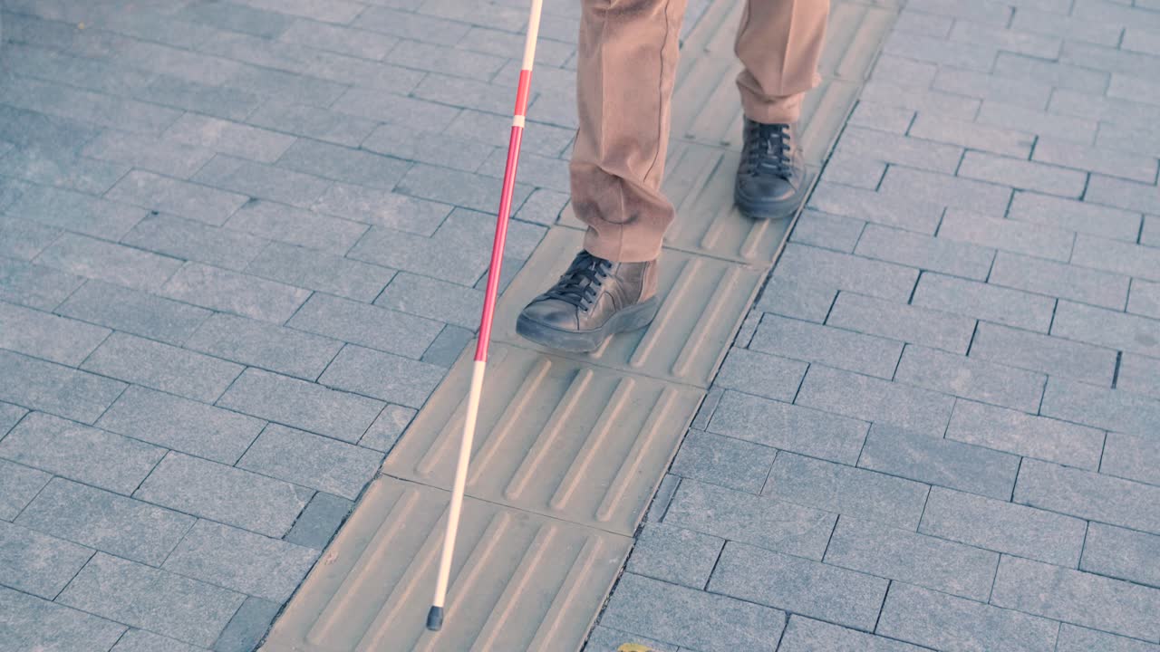 persona ciega usando bastón blanco en azulejos táctiles rectos para navegar por la carretera